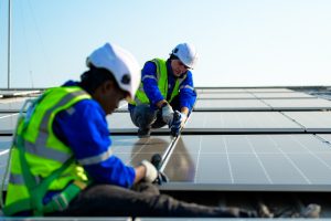 Two workers in safety vests and helmets install solar panels on a rooftop under clear skies, showcasing professional Solar Panel Installation in Lafourche Parish.