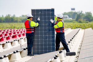 Two workers in safety gear perform a Solar Panel Installation in East Baton Rouge Parish, with rows of panels and red barriers visible in the background.
