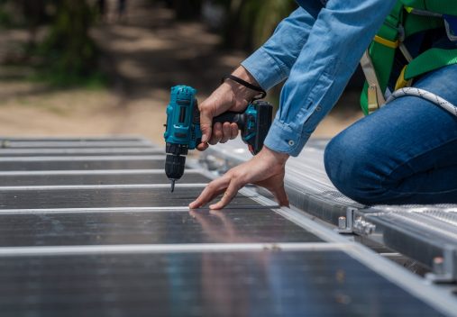 Wearing safety gear, a person uses a power drill to install or secure a solar panel outdoors during a Solar Panel Installation in East Baton Rouge Parish.