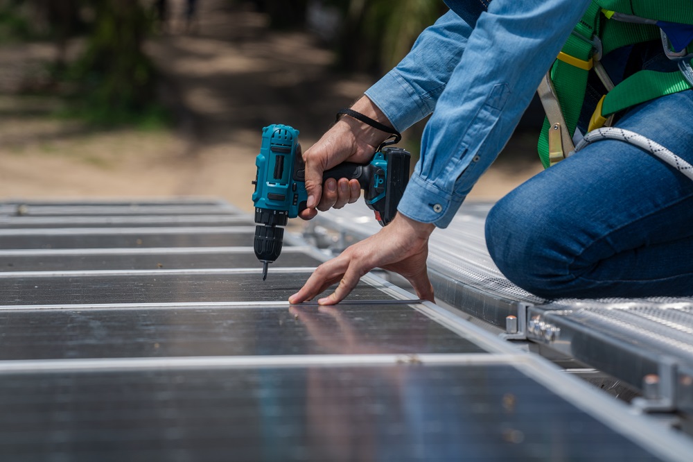 Wearing safety gear, a person uses a power drill to install or secure a solar panel outdoors during a Solar Panel Installation in East Baton Rouge Parish.