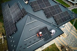 Aerial view of Solar Installers in Tangipahoa Parish fitting solar panels on a residential metal roof, with several panels already secured and tools visible nearby.